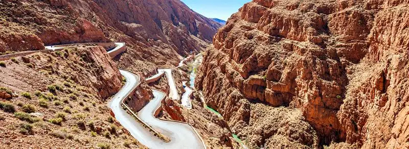 Morocco road trip: A road winding in tight hairpin bends up a red rock gorge in the Dades Valley, with a thin green river far below