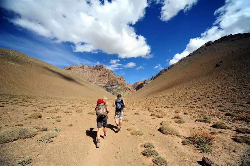 Hikers in a wide High Atlas valley below rocky cliffs, on the way to the canyons