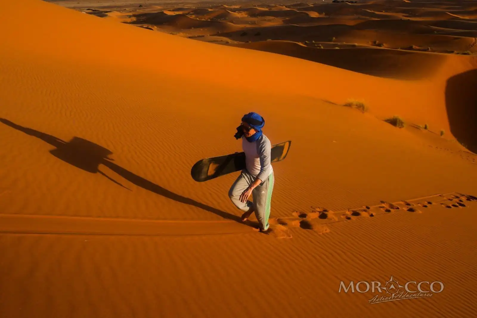 Sandboarding in Morocco: a rider slides down an Erg Chebbi dune in Merzouga, with two quads parked on the crest