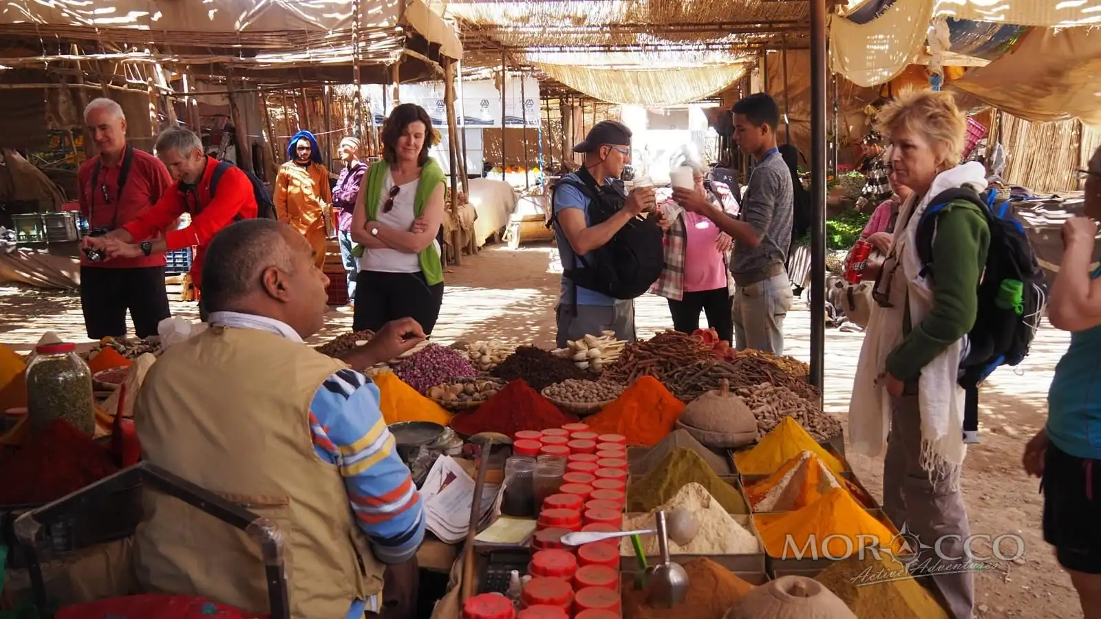 Travellers shopping at a spice stall in a Moroccan souk, the kind of market visit that starts a cooking class in Marrakech